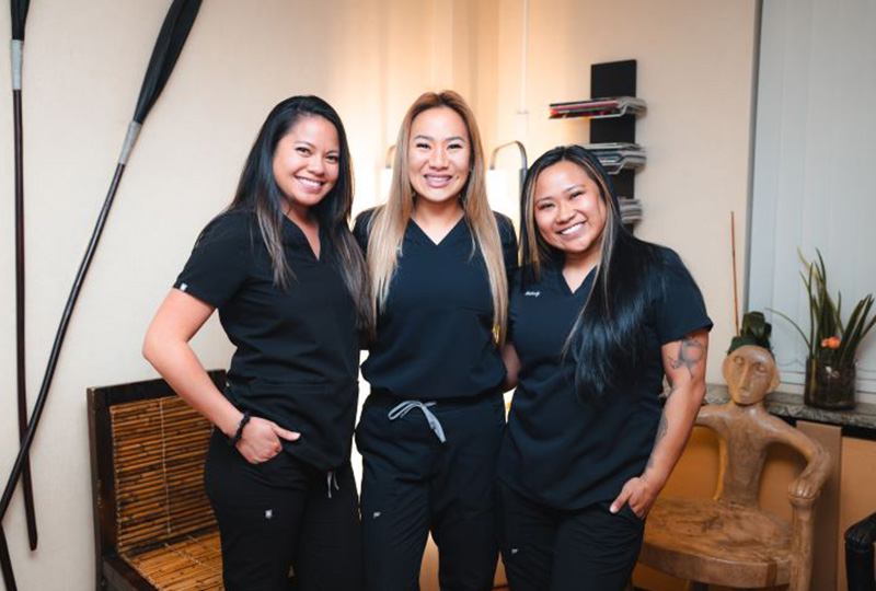A group of five individuals, possibly dental professionals, in a dental office setting, celebrating with raised hands and thumbs up.